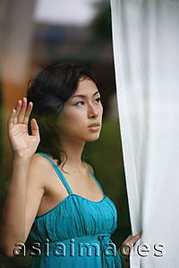 Asia Images Group - Woman looking through window, holding curtain