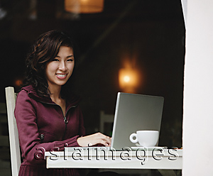 Asia Images Group - Woman sitting in cafe working on laptop, looking at camera, smiling