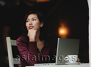 Asia Images Group - Woman sitting in cafe working on laptop, looking away