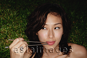 Asia Images Group - woman holding chopsticks up to mouth, looking out of corner of eye