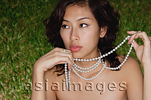 Asia Images Group - Woman holding strand of necklace, looking away from camera