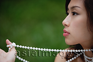 Asia Images Group - woman holding necklace and looking away from camera