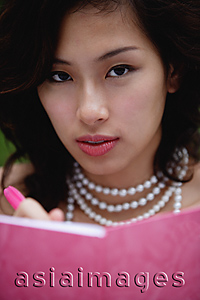 Asia Images Group - Woman wearing necklace and writing in pink journal, looking at camera