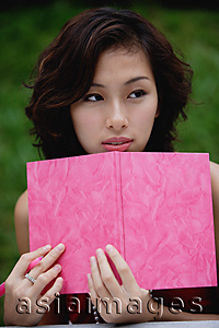 Asia Images Group - Woman sitting in cafe holding pink journal and pink pen, looking away from camera