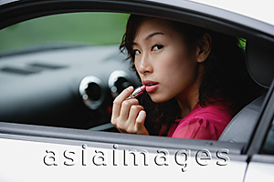Asia Images Group - Woman sitting in car, applying lipstick, looking over shoulder out window