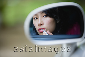 Asia Images Group - Woman applying lipstick in side view mirror of car