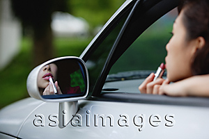 Asia Images Group - Woman applying lipstick in side view mirror of car, while in driver's seat