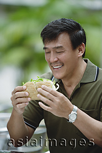 Asia Images Group - Man sitting in outdoor cafe eating sandwich