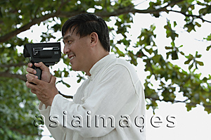 Asia Images Group - Man in park using super 8 movie camera