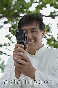 Asia Images Group - Man in park using super 8 movie camera, looking at camera