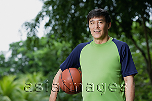 Asia Images Group - Man playing basketball, holding ball, in park
