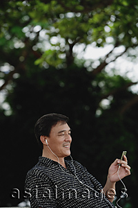 Asia Images Group - Man sitting in park, listening to music on MP3 player