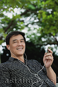 Asia Images Group - Man sitting in park listening to MP3 player, smiling