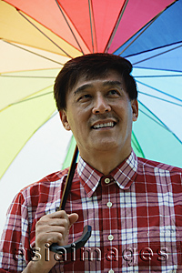 Asia Images Group - Man standing under rainbow umbrella, smiling