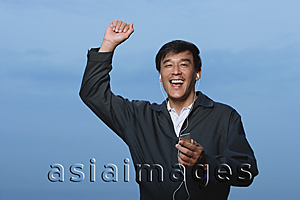Asia Images Group - Man walking and listening to music on MP3 player, arm raised in air