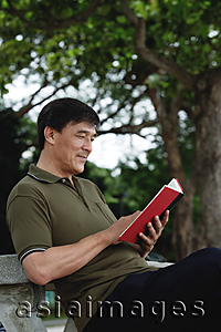 Asia Images Group - Man sitting on bench in park reading