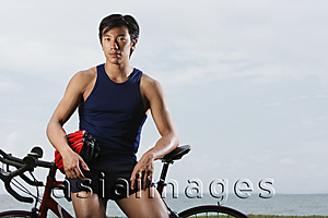 Asia Images Group - Man resting on bike along ocean, looking at camera