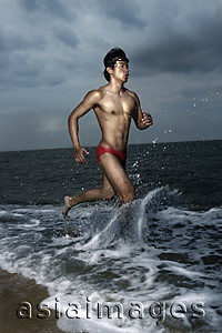 Asia Images Group - Muscled man wearing swim trunks, running along ocean