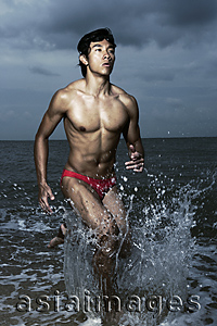 Asia Images Group - Muscled man wearing swim trunks, running out of ocean, triathlon, race
