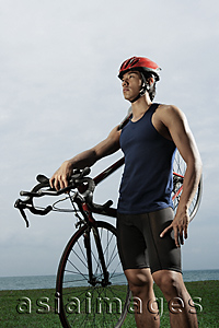 Asia Images Group - Man holding bike along ocean, wearing helmet, workout