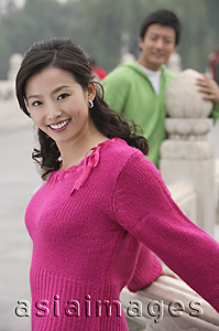 Asia Images Group - A woman smiles at the camera as her boyfriend stands in the background