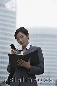 Asia Images Group - A businesswoman looks at the camera as she uses her cellphone