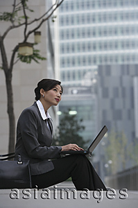 Asia Images Group - A businesswoman sits down and uses her laptop