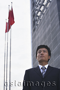 Asia Images Group - A businessman stands in front of a building with flags