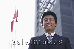 Asia Images Group - A businessman looks at the camera as he stands in front of a building with flags