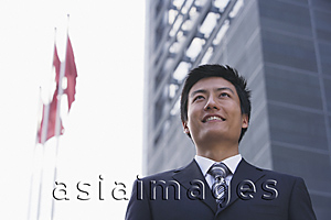 Asia Images Group - A businessman stands in front of a building with flags