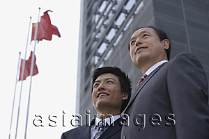 Asia Images Group - Two businessmen stand in front of a building with flags