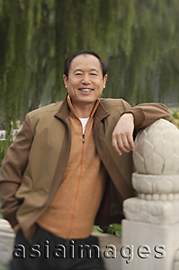 Asia Images Group - A man smiles at the camera as he leans on a stone post