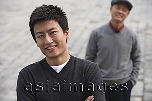 Asia Images Group - A man looks at the camera as his grandfather stands in the background