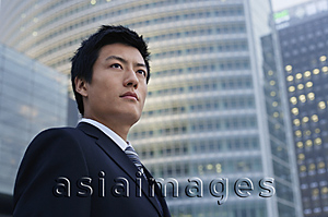 Asia Images Group - A businessman stands in front of a skyscraper