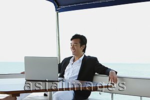 Asia Images Group - Young man on yacht, using laptop