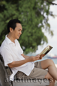 Asia Images Group - Man at the beach, sitting on a bench and reading a book
