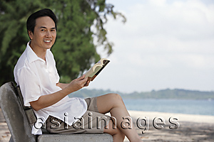 Asia Images Group - Man at the beach sitting on a bench, looking at camera
