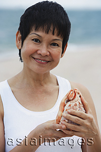 Asia Images Group - Woman with sea shell at the beach, smiling at camera
