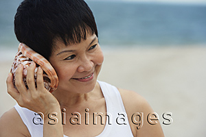 Asia Images Group - Woman at the beach listening to sea shell