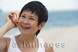 Asia Images Group - Woman at the beach listening to sea shell