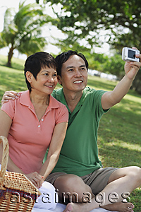 Asia Images Group - Mature couple having a picnic in the park and taking a picture of themselves