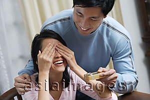 Asia Images Group - Young woman covering her eyes while man is giving her a present