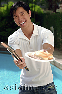 Asia Images Group - Young man offering hot dog and smiling at camera