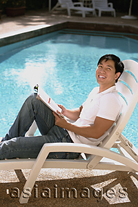 Asia Images Group - Young man relaxing in deck chair by the pool