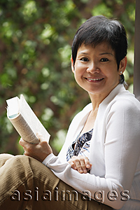 Asia Images Group - Woman relaxing with book in the garden and smiling at camera