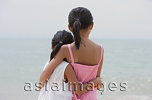 Asia Images Group - Young sisters hugging and looking out at sea