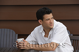 Asia Images Group - Young man sitting at table looking over his shoulder