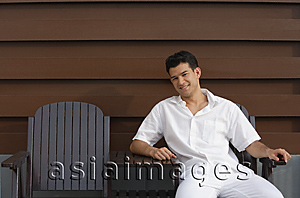 Asia Images Group - Young man sitting in garden chair and looking at camera