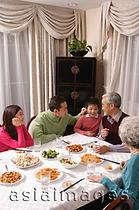 Asia Images Group - Family at dinner table having traditional food, boy standing next to grandfather