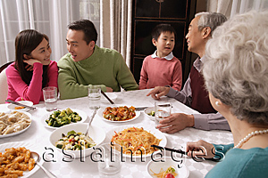 Asia Images Group - Family chatting over at dinner table having traditional food, boy standing next to grandfather